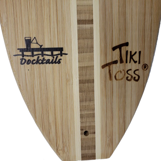 Close-up of a bamboo-style surfboard blank with visible grain, a vertical center stripe, and printed logos reading Docktails and Tiki Toss.