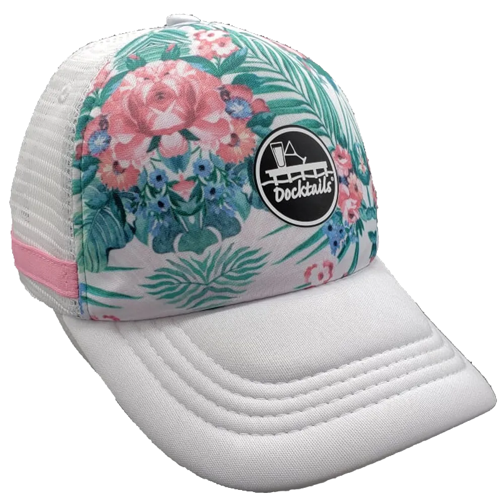 A white trucker hat with a tropical floral and palm leaf pattern on the front panel, a white mesh side panel with a pink fabric band, and a black circular 'Docktails' logo patch on the crown.