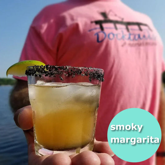 Man holding a mixed drink in a glass with black salt and a lime wedge on the rim