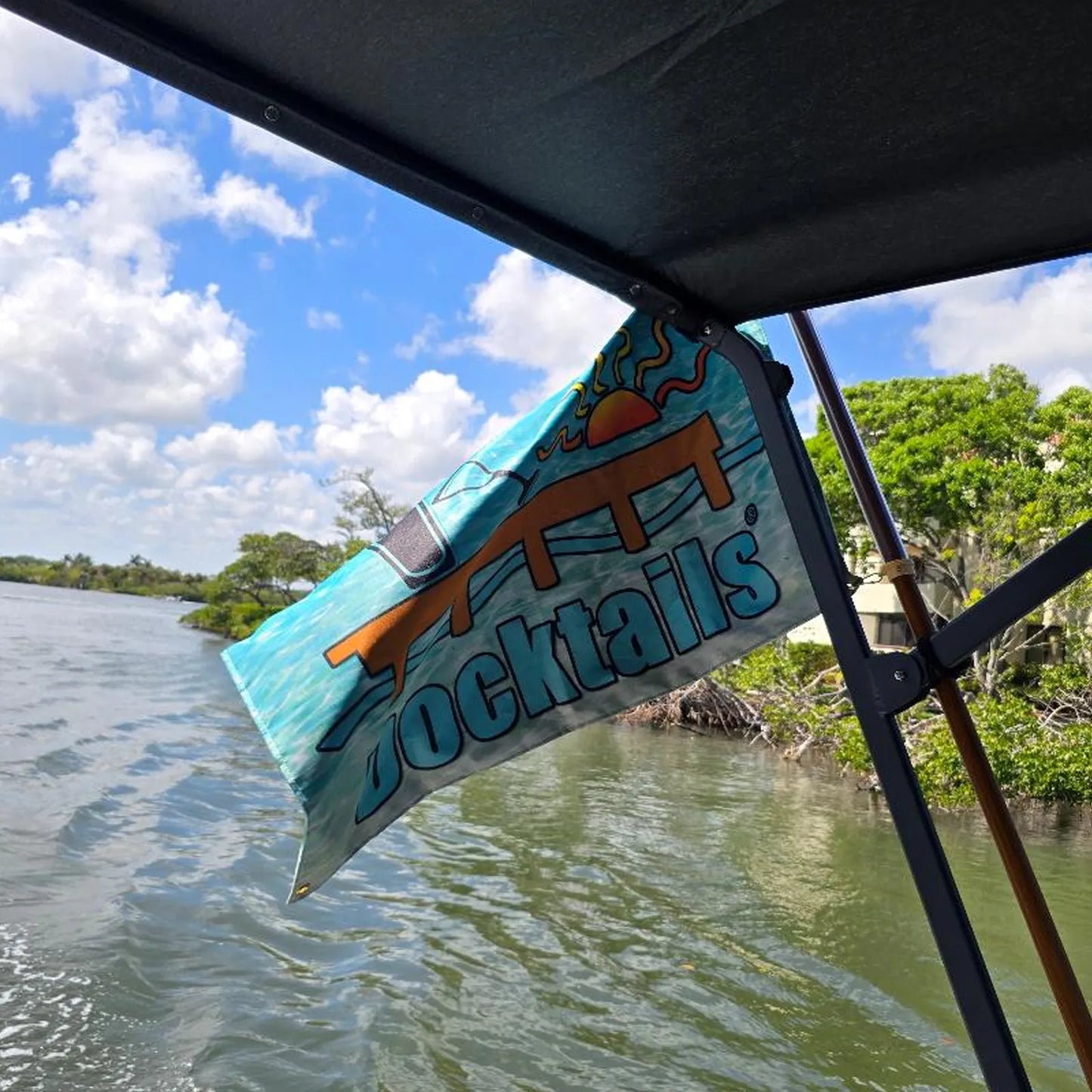 Boat flag with the word Docktails and a dock, with a sun, and portions of a martini glass and a pint glass. Flag is flying from a boat, and shows water in the background.