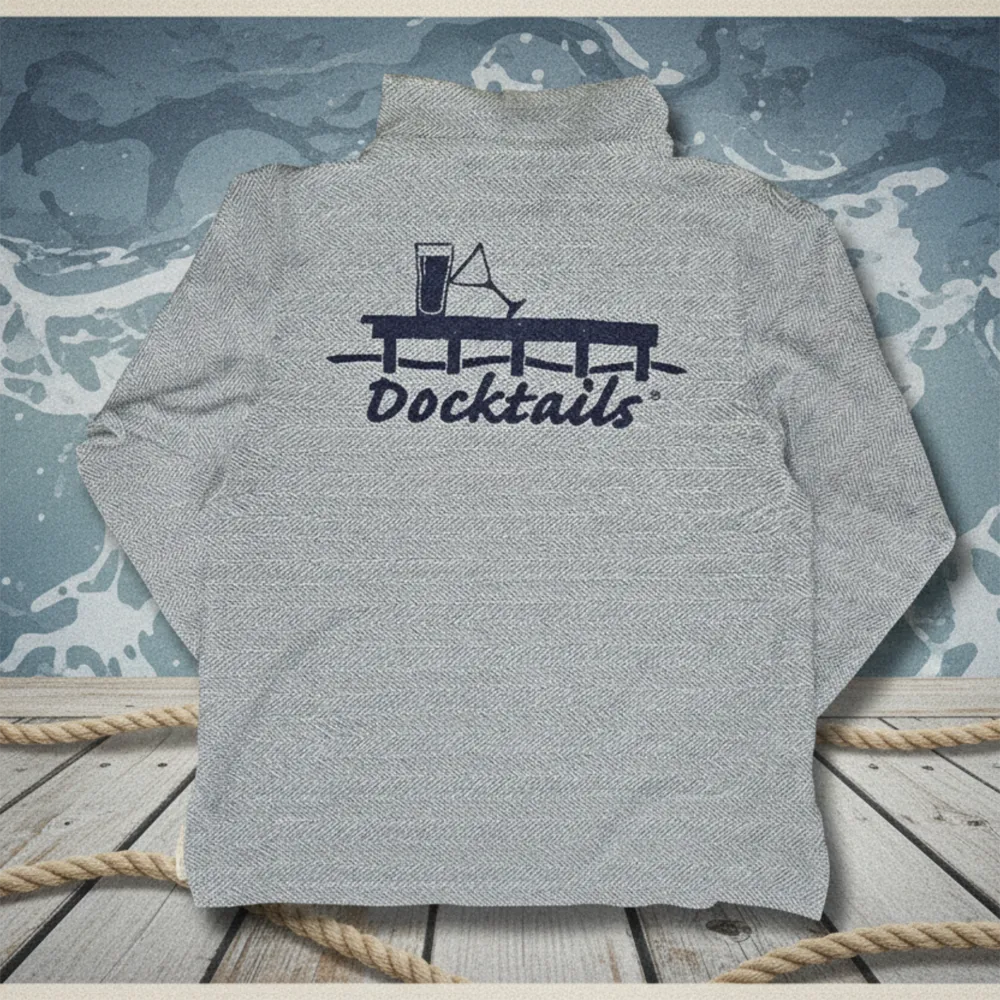 The back of a heather blue hoodie with a dark navy graphic reading 'Docktails' under a cocktail glass and dock, displayed on a wooden surface with rope and a blue marbled backdrop.