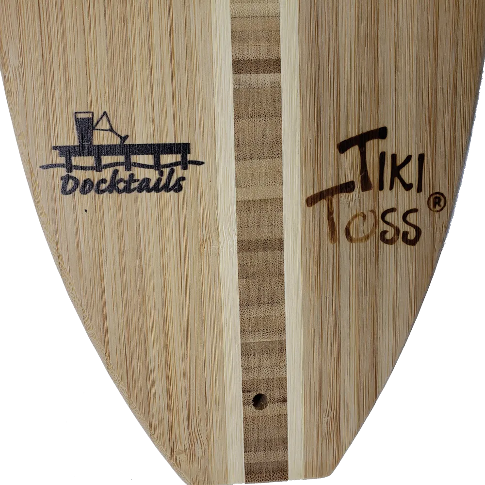Close-up of a bamboo-style surfboard blank with visible grain, a vertical center stripe, and printed logos reading Docktails and Tiki Toss.