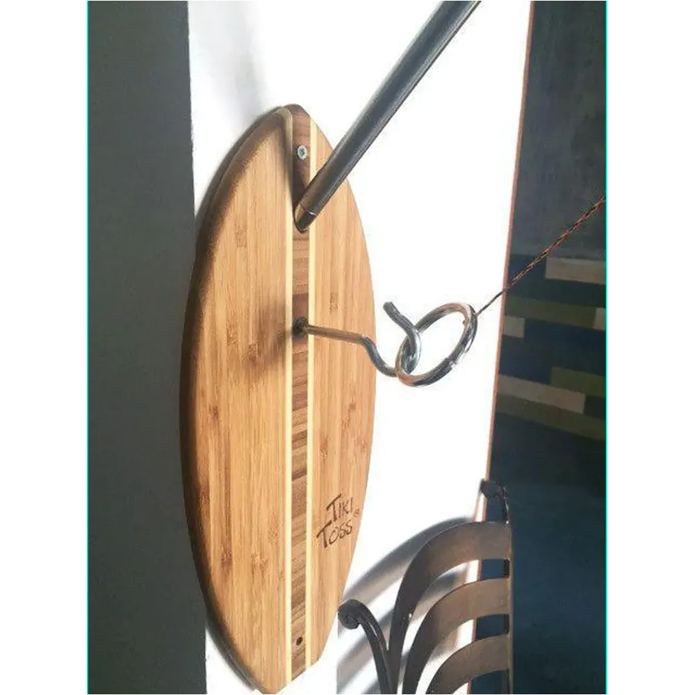 Surfboard shaped wooden game hanging on a wall with a pole, a hook and ring, and a chair.