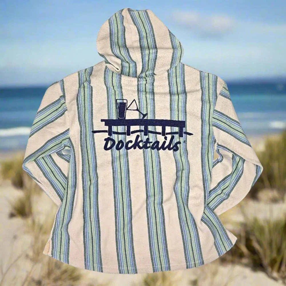A hooded long-sleeve shirt with vertical blue and green stripes on an off-white background, featuring a dark blue 'Docktails' graphic with a cocktail and martini glass on the back. The shirt is displayed against a blurred beach background.