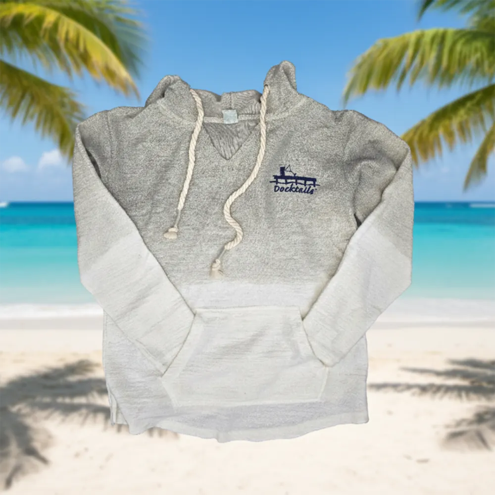 A heather beige hoodie with a white gradient fade on the sleeves and lower body, featuring a navy blue 'Docktails' logo on the left chest. The hoodie is shown against a tropical beach backdrop with palm trees and turquoise water.