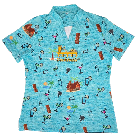 A women's short-sleeve collared golf polo shirt in a heathered light blue color, featuring an all-over tropical cocktail and beach hut pattern. The center chest features a yellow and orange graphic that reads 'Docktails'.